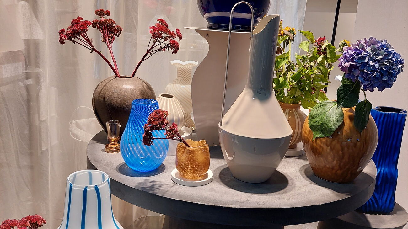 Arrangement aus Glasvasen in Blitzblau und Creme mit Blüten, auf verschieden hohen Beistelltischen
