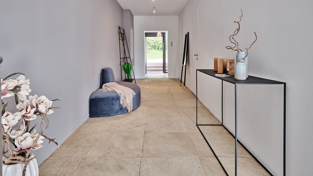 Langer Flur mit Steinboden und Samtbank in blau sowie Metallkonsole und Anlehngarderobe in Schwarz