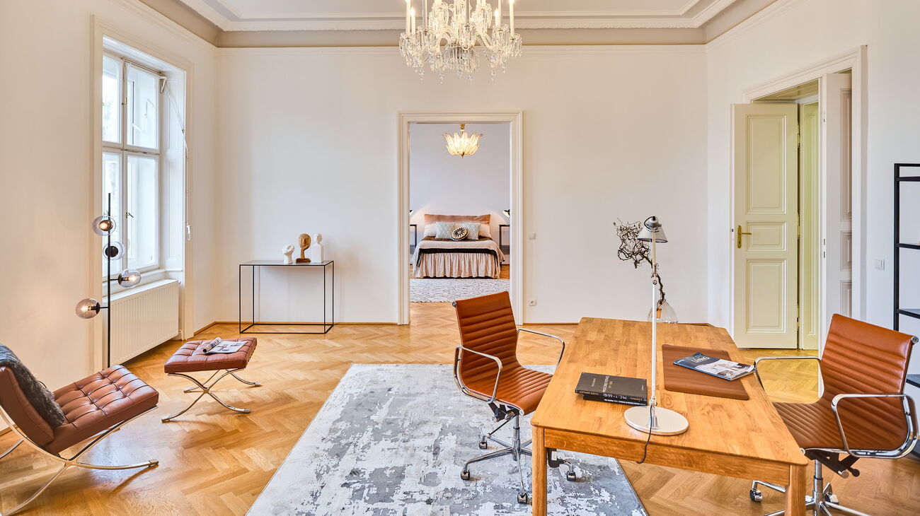 großer Raum mit Luster, Schreibtisch aus Holz, Ledersessel in braun und Teppich in grau