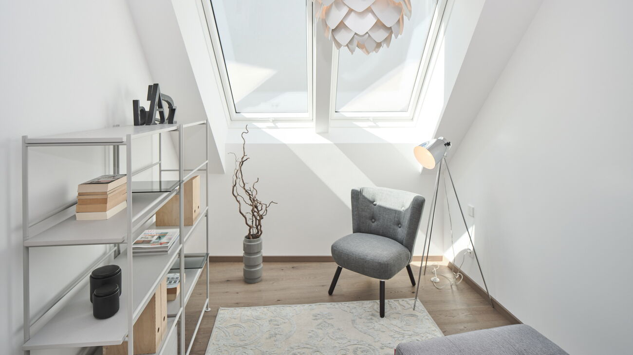 Gästezimmer mit grauem halbhohem Bücherregal, grauem Loungestuhl, silberner Schuppenleuchte, grauem Daybed und silbernem kurzflorigen Teppich