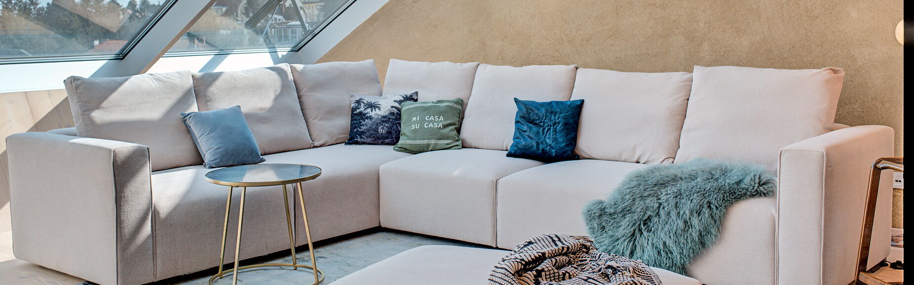 Sofa-Landschaft in cremefarbenem Stoff mit blauem Teppich im Dachgeschoß