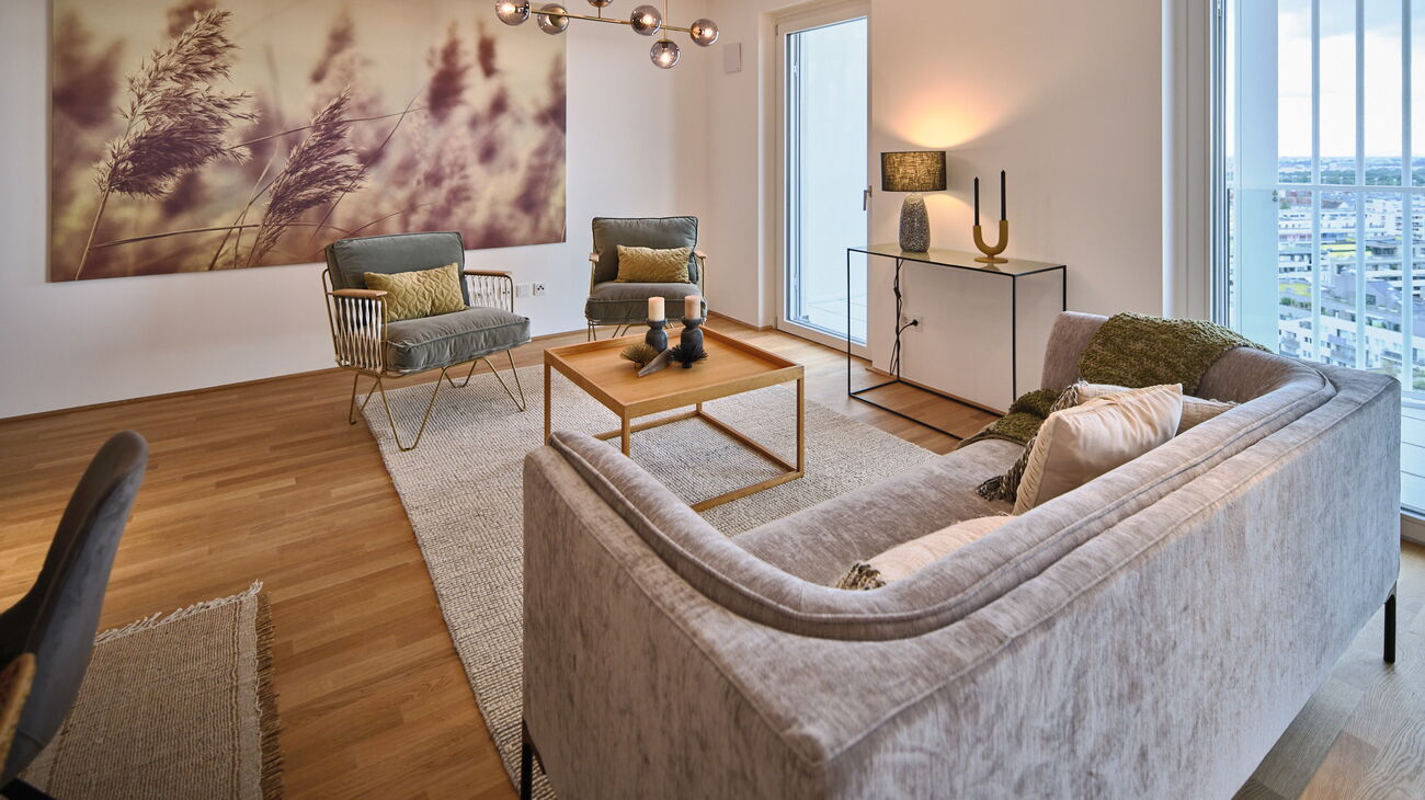 graues Samtsofa und 2 graue Samt-Lounger mit goldigem Metall-Rahmen, heller Wollteppich und Metall Couchtisch und übergroßes Leinenbild mit Ähren