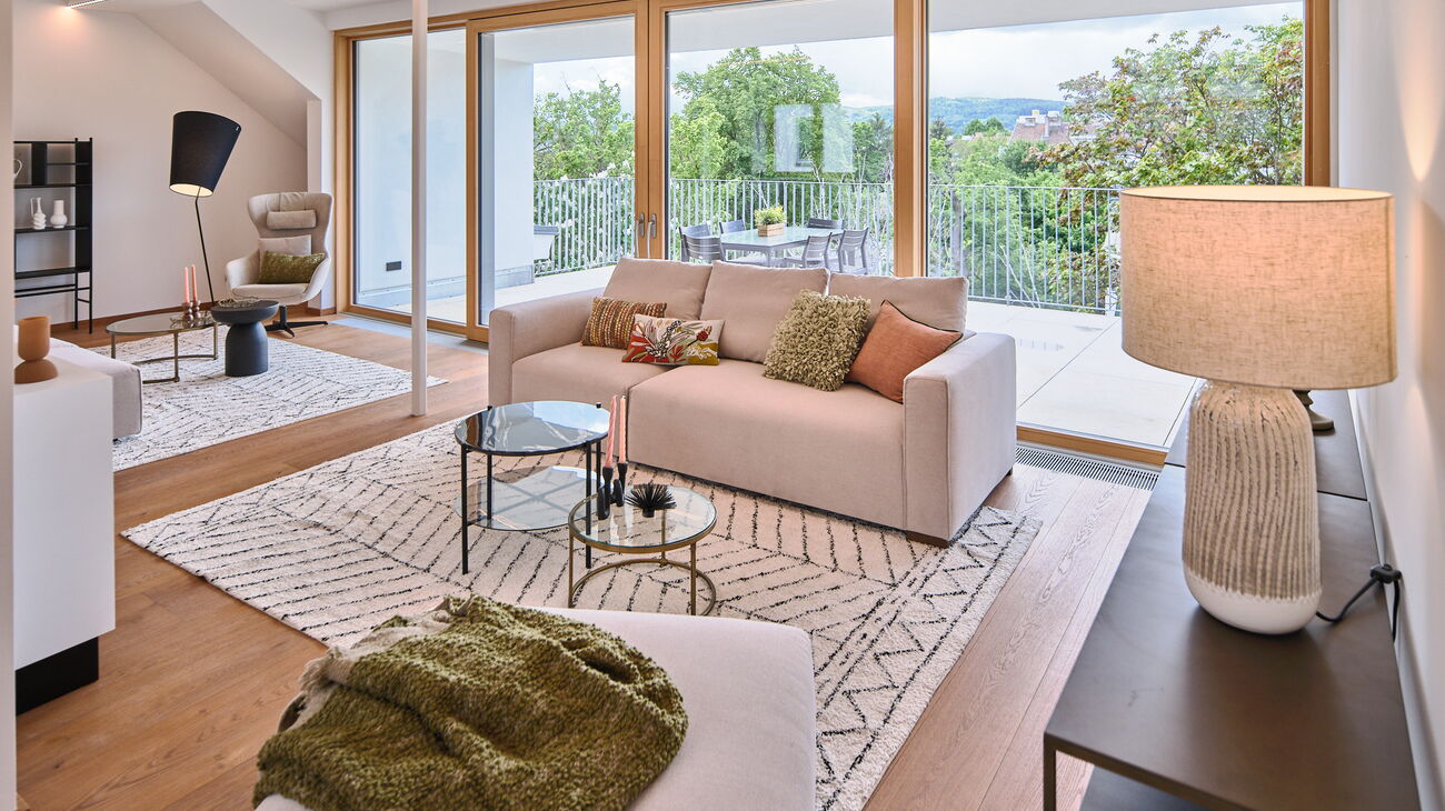 Blick ins Wohnzimmer mit Terrasse dahinter - cremefarbenes Modulsofa schwarze Konsole heller Teppich Tischleuchte und Couchtisch-Set