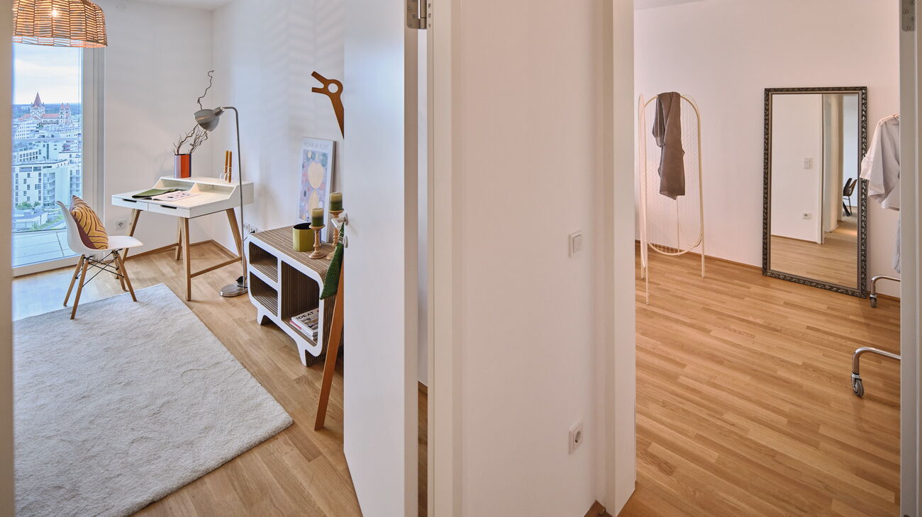 Blick vom Gang Richtung Arbeitszimmer und danebenliegendem Schlafzimmer - kleiner Home Office Bereich mit Schreibtisch und Stuhl, daneben Standgarderobe mit Deko