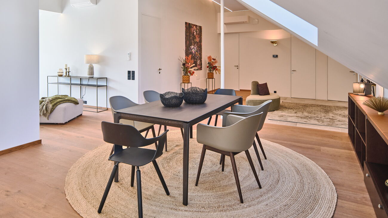 offener Essplatz mit Blick in den Eingangsbereich, dunkler Holztisch mit abgerundeten Ecken, olivgrüne Designstühle mit dunklen Holzbeinen, Sisalteppich, langes Sideboard aus dunklem Holz