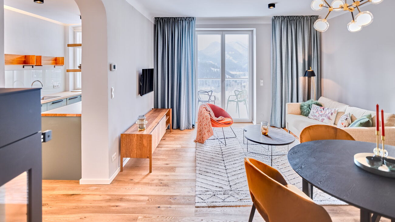 Wohnzimmer mit schwarzem Esstisch, Samtstühlen, Schlafsofa, TV Board, Kuschelteppich und Holzofen