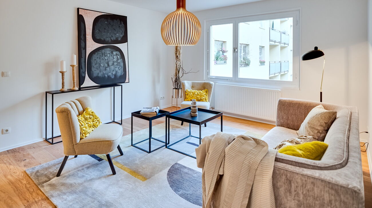 graues Samtsofa gelb-grauer Teppich Design-Deckenleuchte aus Holz Wandbild in schwarz-weiß auf schwarzer Konsole und schwarzes Couchtisch-Set und schwarze Stehleuchte mit Tütenschirm