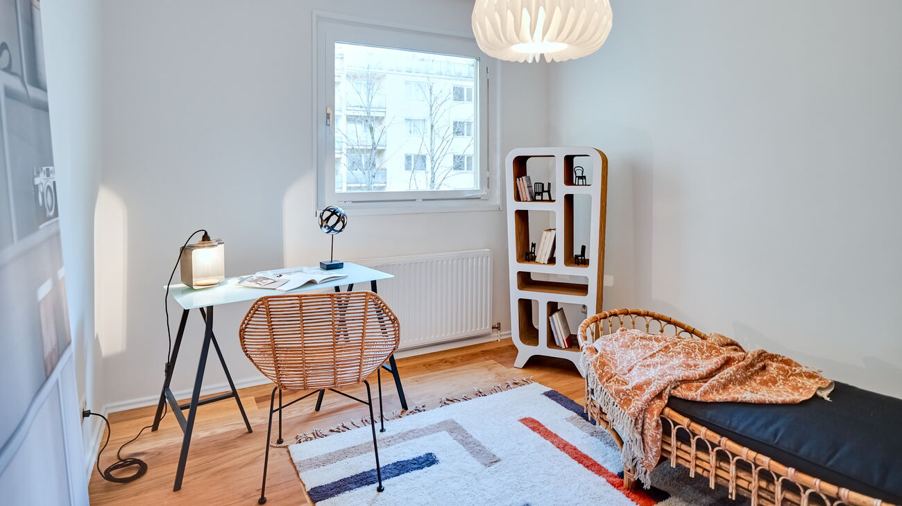 Jugendzimmer oder Gästezimmer mit kleinem Schreibtisch mit Bambusplatte, Rattan-Daybed samt Plaid und Kissen und einem nachhaltigen Karton-Regal und einem bunten Teppich