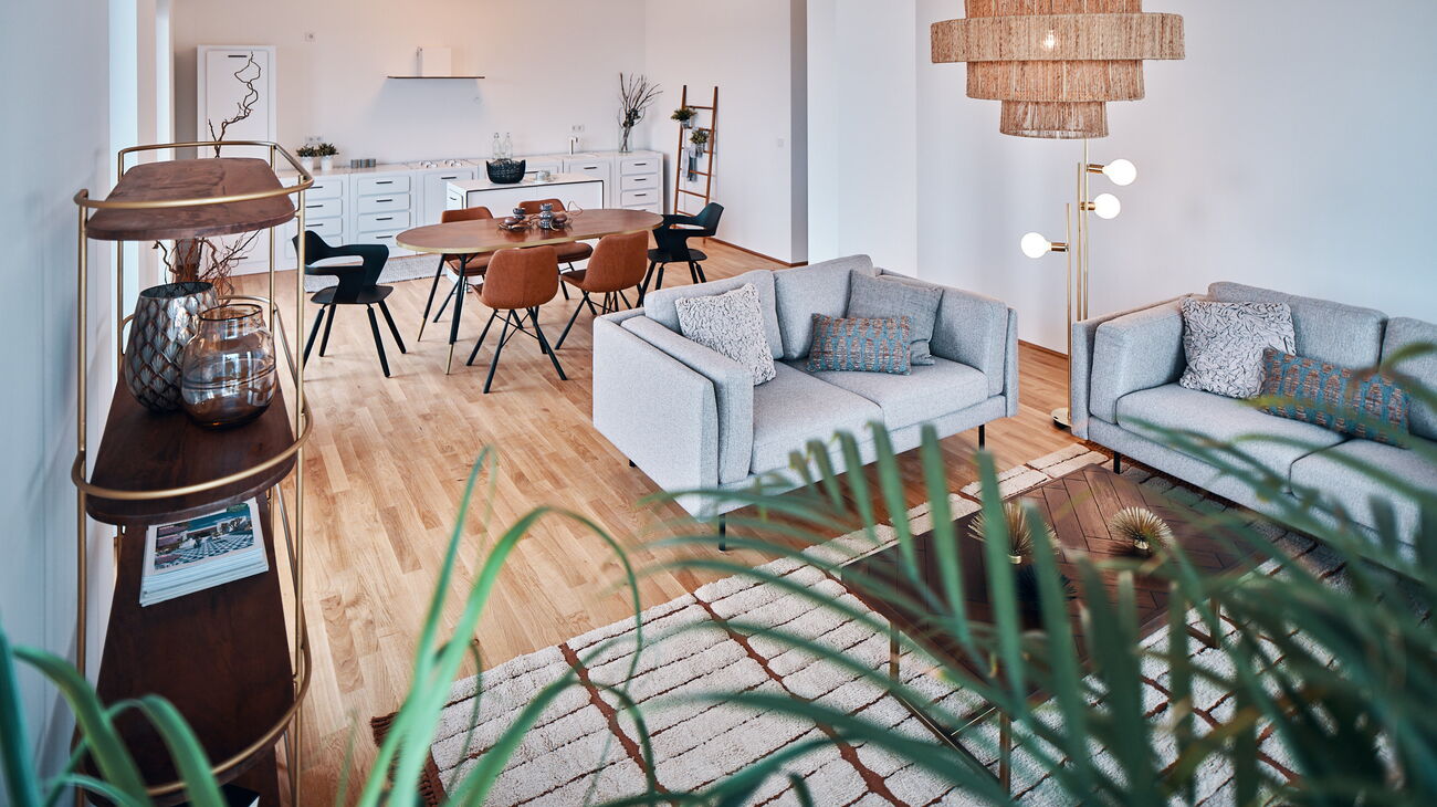 Blick vom Wohnzimmer Richtung Küche mit Esstisch oval aus Holz und 4 Polsterstühlen in braun und 2 Kunststoffstühlen in schwarz sowie 2 weißen schlichten Deckenleuchten