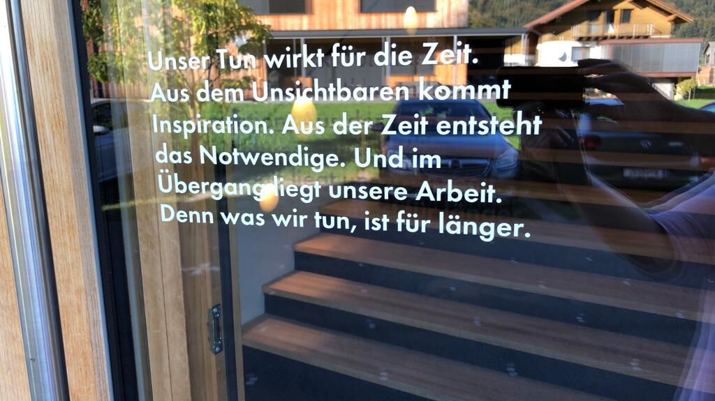 Spruch an der Tür: unser Tun wirkt für die Zeit. Aus dem Unsichtbaren kommt Inspiration. Aus der Zeit entsteht das Notwendige. Und im Übergang liegt unsere Arbeit. Denn was wir tun, ist für länger.